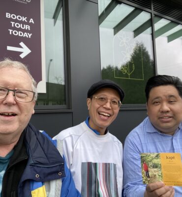 Joe Planta, Dale McGladdery and Roland Tanglao on Kingsway in Vancouver just east of Analog Coffee at an outdoor pseudo-patio. Covered! Joe is holding up a marketing postcard for kapé which is a social venture promoting ethically sourced, farmer-first, direct trade coffee from Philippine Indigenous growers and batch roasted on unceded Coast Salish Territories (Vancouver, Canada).